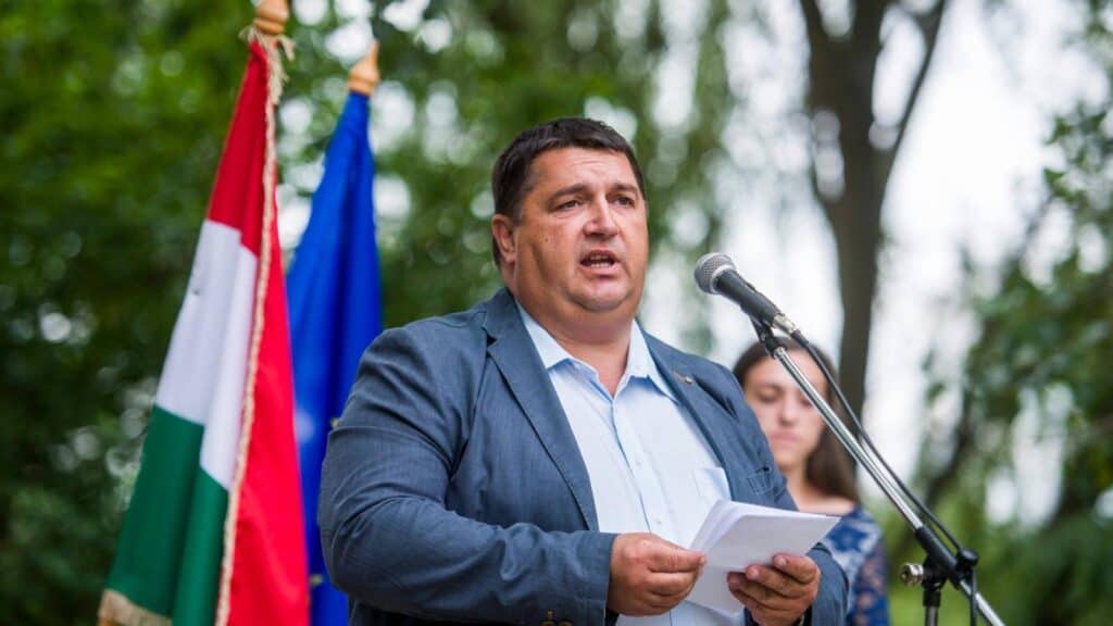 Politikus beszédet mond egy kültéri eseményen, mögötte magyar és uniós zászlók láthatók.